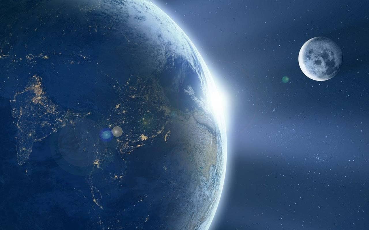 A view of the Earth and the Moon from outer space, as the sun rises around the edge of the planet.