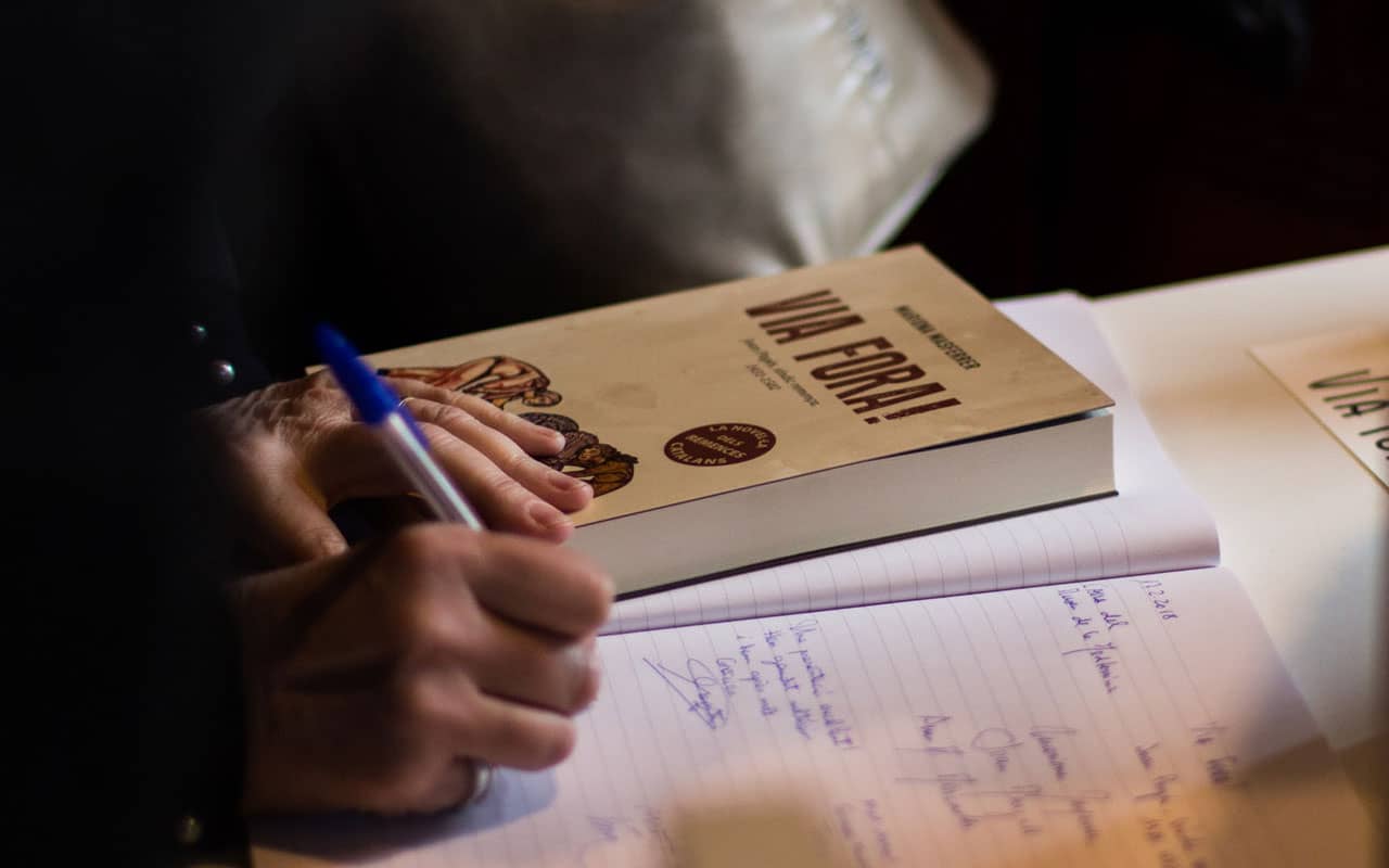 A person writes in a lined notebook with a copy of Via Fora! sitting beside them. Reading in Spanish is another great way to learn the language.