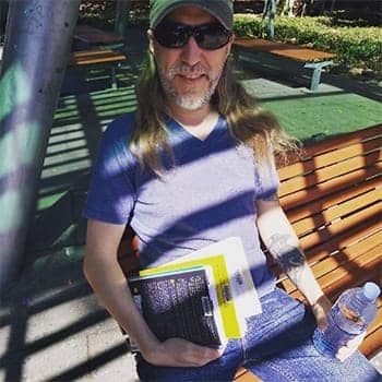 Books on learning feature image of Anthony Metivier on a bench with a pile of books