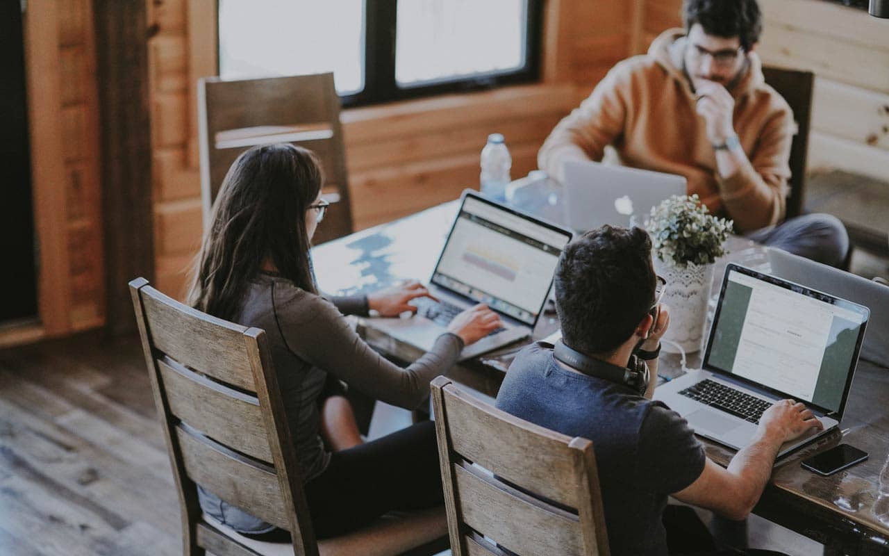 A group of three people sit around a table with their laptops. You could use an in-person accountability group to help you study effectively.