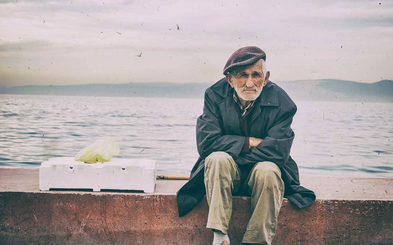 An old man sits on a sea-wall.