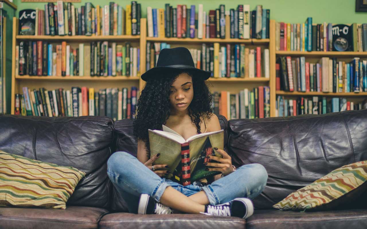 A woman reads a book on a couch in a library.