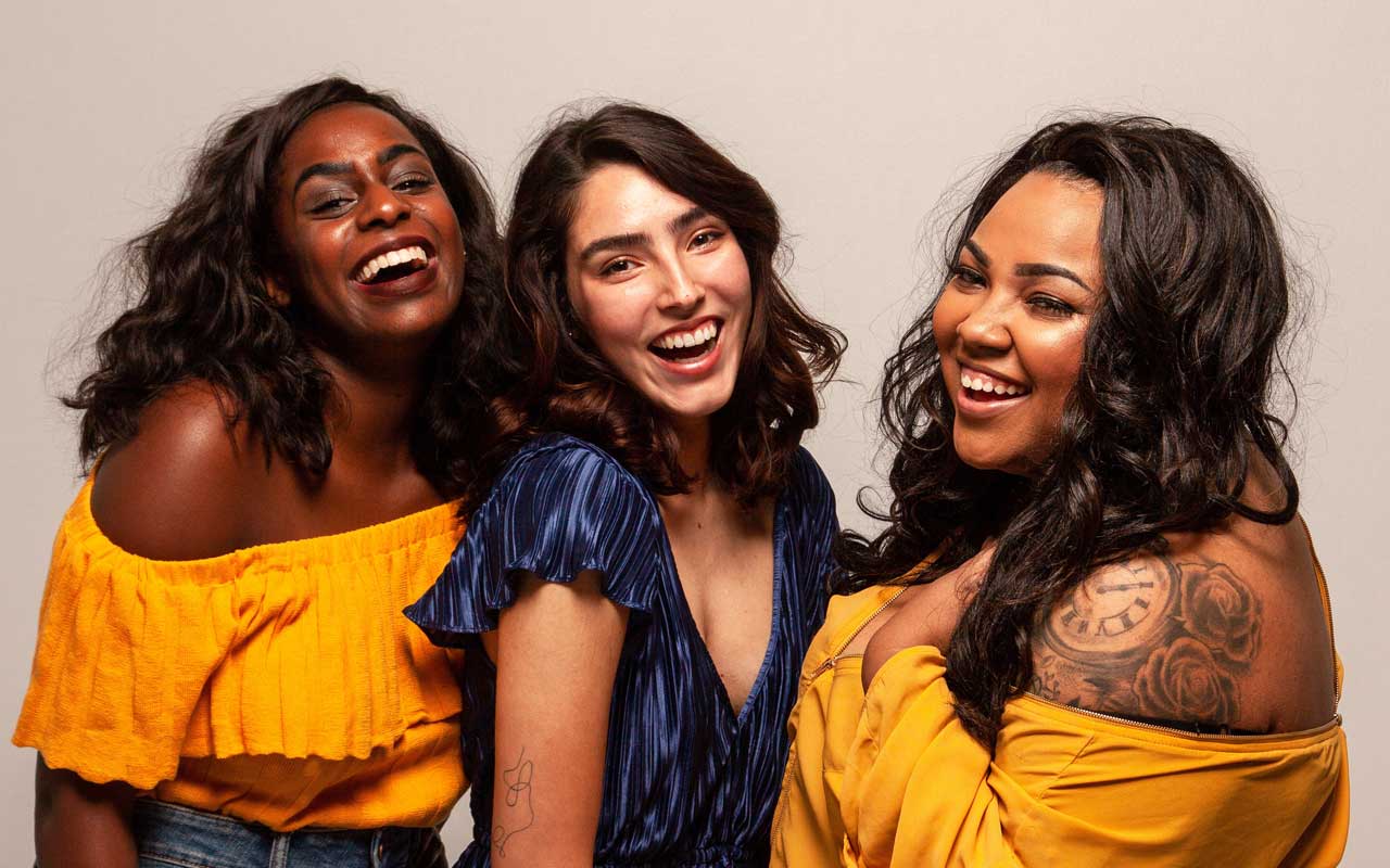 Three women are dressed up to go out, stand laughing. Socialization can help improve memory.