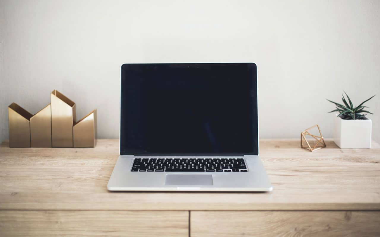 A laptop sits on top of a wooden desk with a few decorative items. Language learning software may be helpful as you learn Spanish.