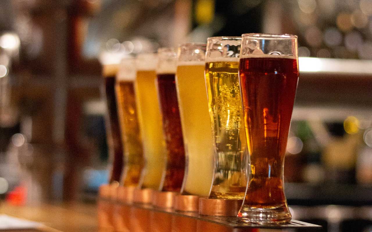 A flight of 7 different craft beers sits on a table.